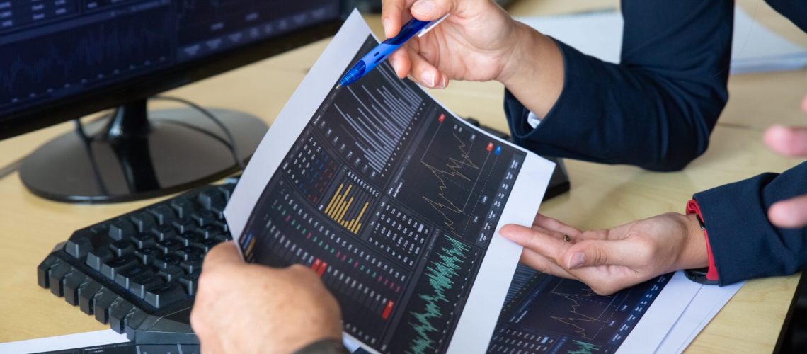 Brokers discussing trading strategy, holding papers with financial data, pointing pen at charts. Cropped shot. Broker job or stock market exchange concept